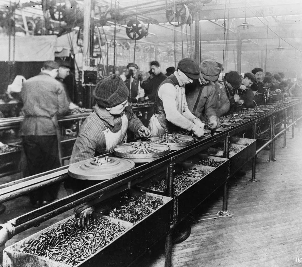 A black and white photograph of men working on an old car assembly line